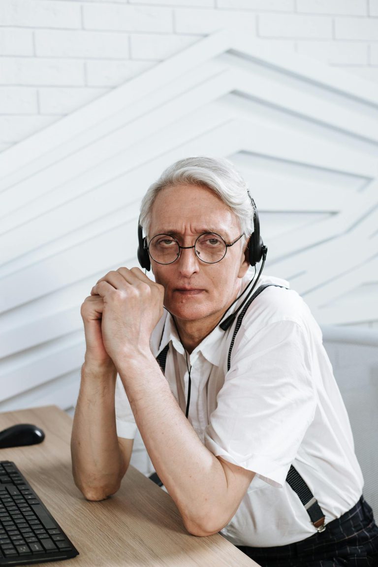 Portrait of a senior call center agent wearing glasses and a headset, engaged at work.